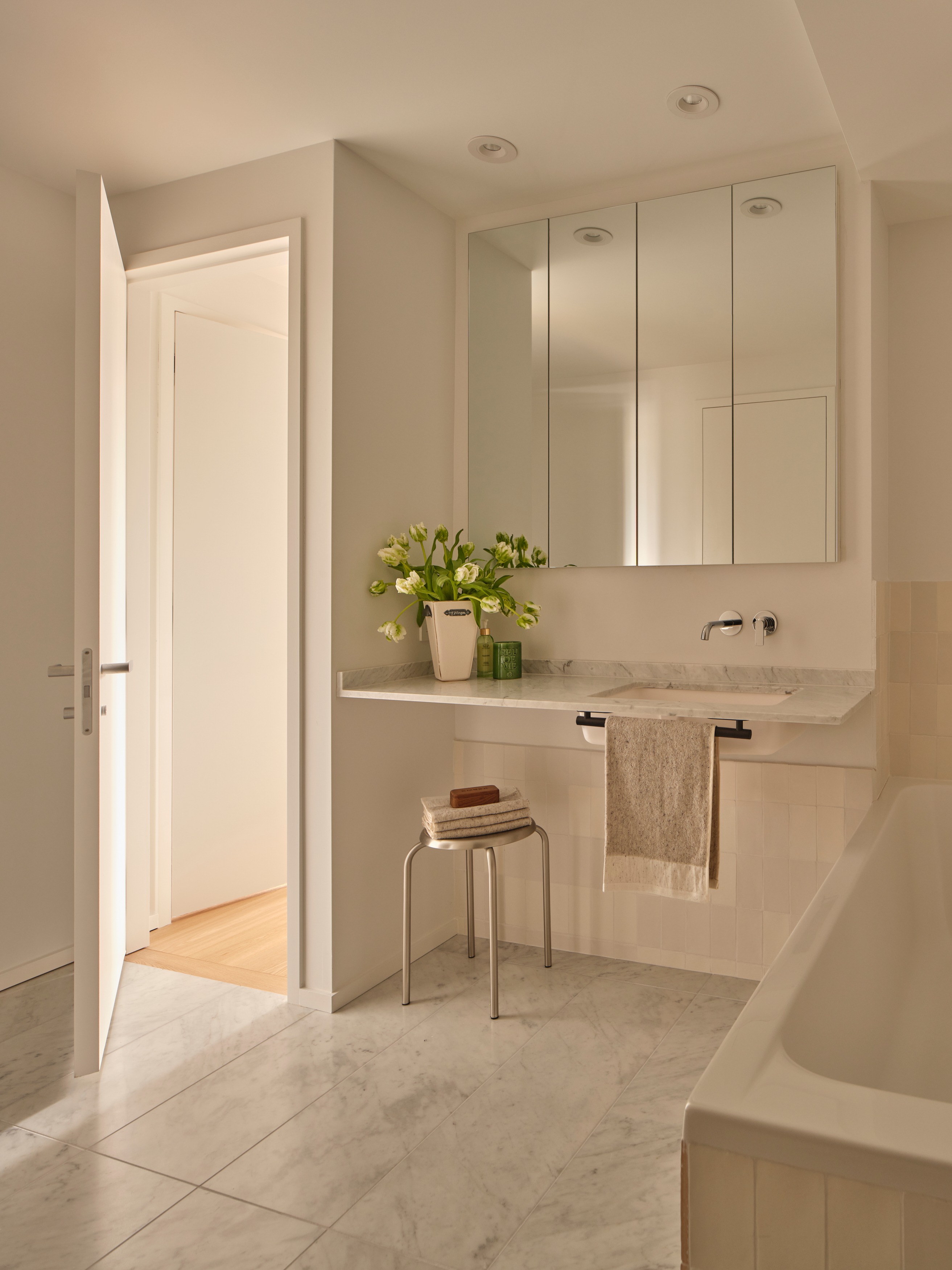 Bathroom with mirrored medicine cabinet, marble vanity, white tulips, and steel stool
